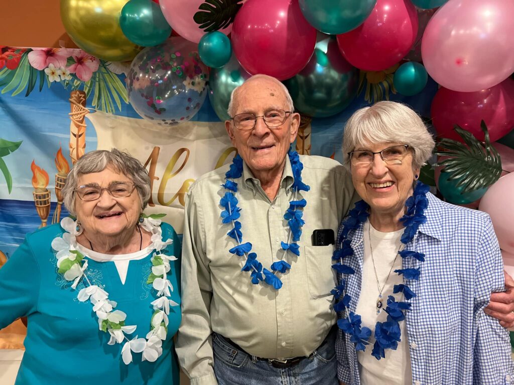 Three residents enjoying a festive event with leis and balloons