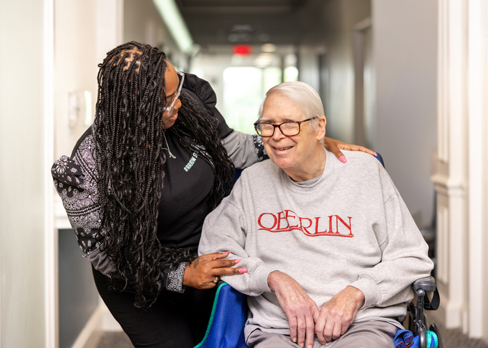 A staff member assisting a smiling resident in a long hallway