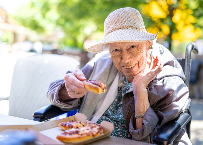 Resident enjoying pizza outdoors with a smile