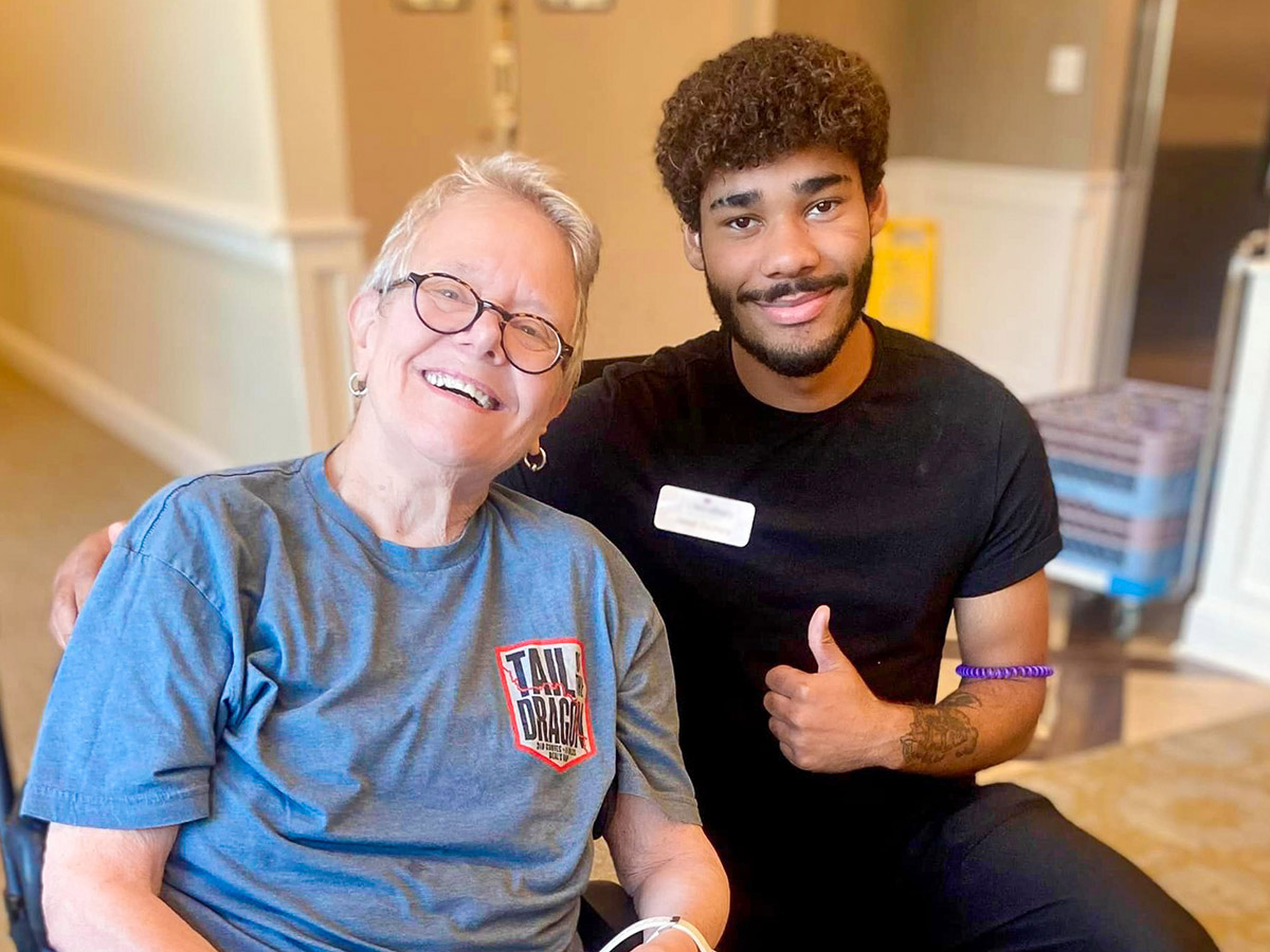 A senior resident smiling with staff in a hallway