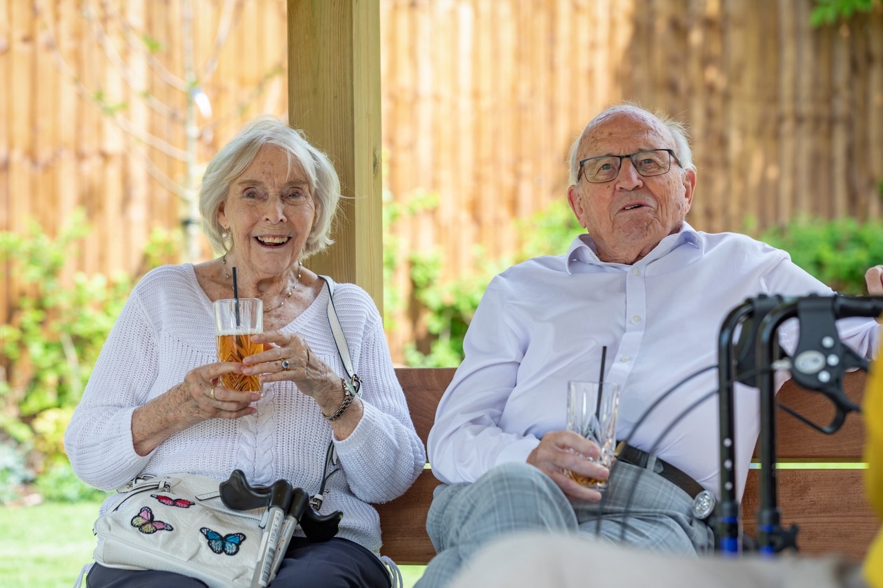 Two seniors enjoying drinks under a shaded area