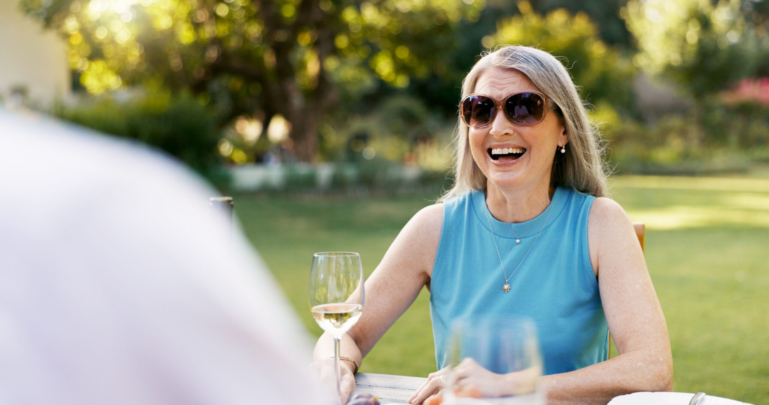 A joyful senior woman laughing outdoors with a drink