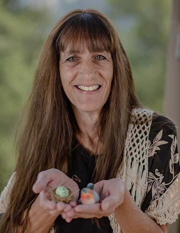 A woman smiling while holding painted stones outdoors