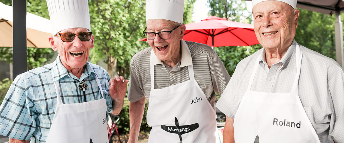 Three residents in chef hats smiling outdoors