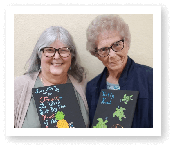 Two women holding decorated boards with colorful messages.