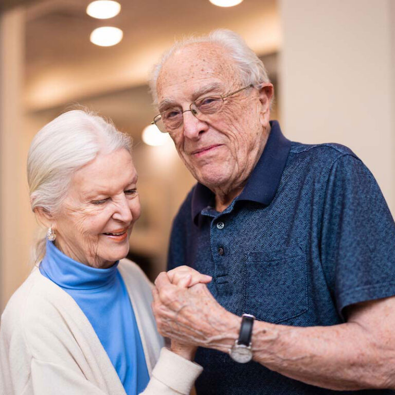Elderly couple smiling and holding hands indoors