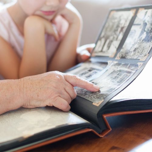 An elderly hand pointing at photos in an album with a child nearby.