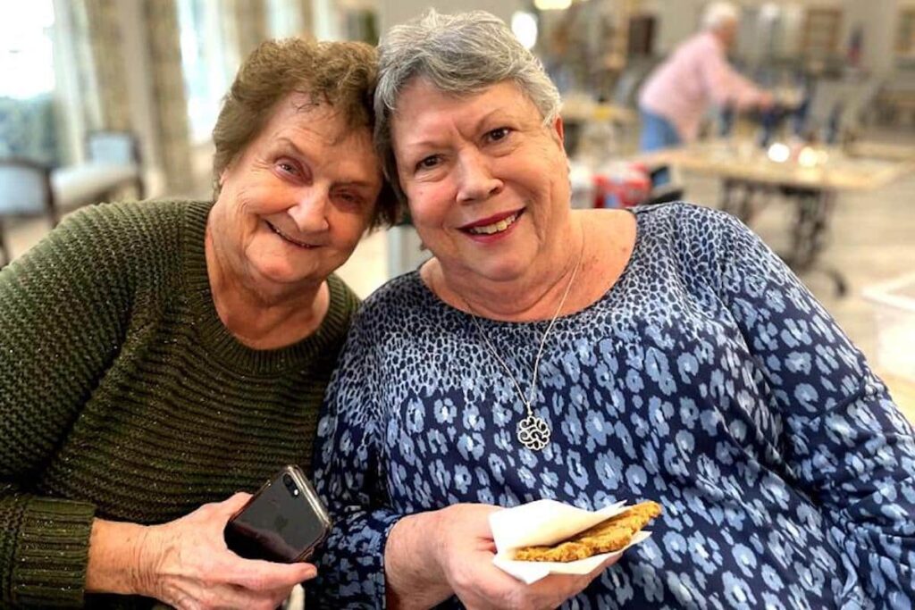 Two smiling women enjoying snacks in a common area.