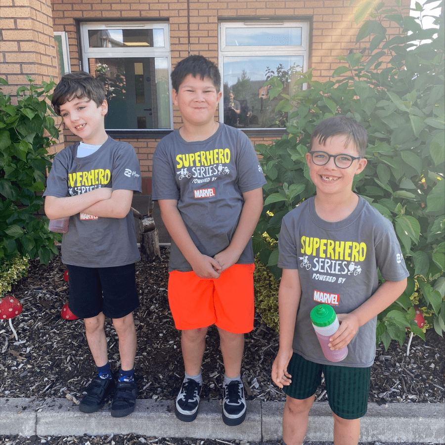 Three children wearing superhero t-shirts in a garden area.