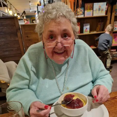 Smiling senior woman enjoying dessert at a table.