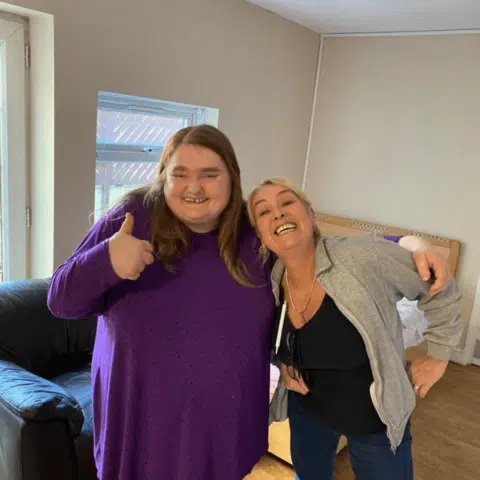 Two women smiling and posing in a facility room.
