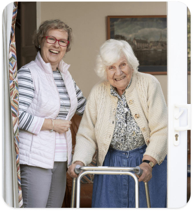 Caregiver smiling with an elderly resident at the door.