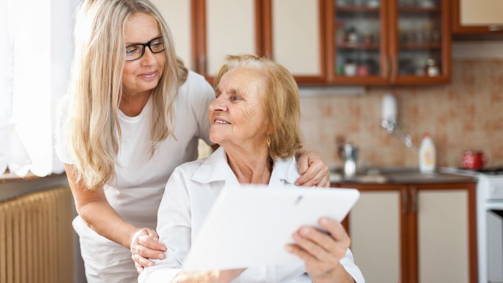 Caregiver assisting an elderly woman with a tablet