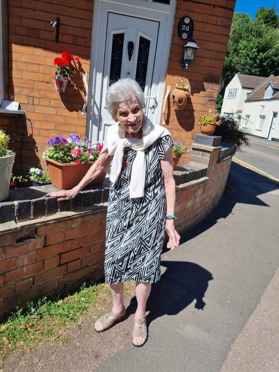 A smiling elderly woman in a garden setting.