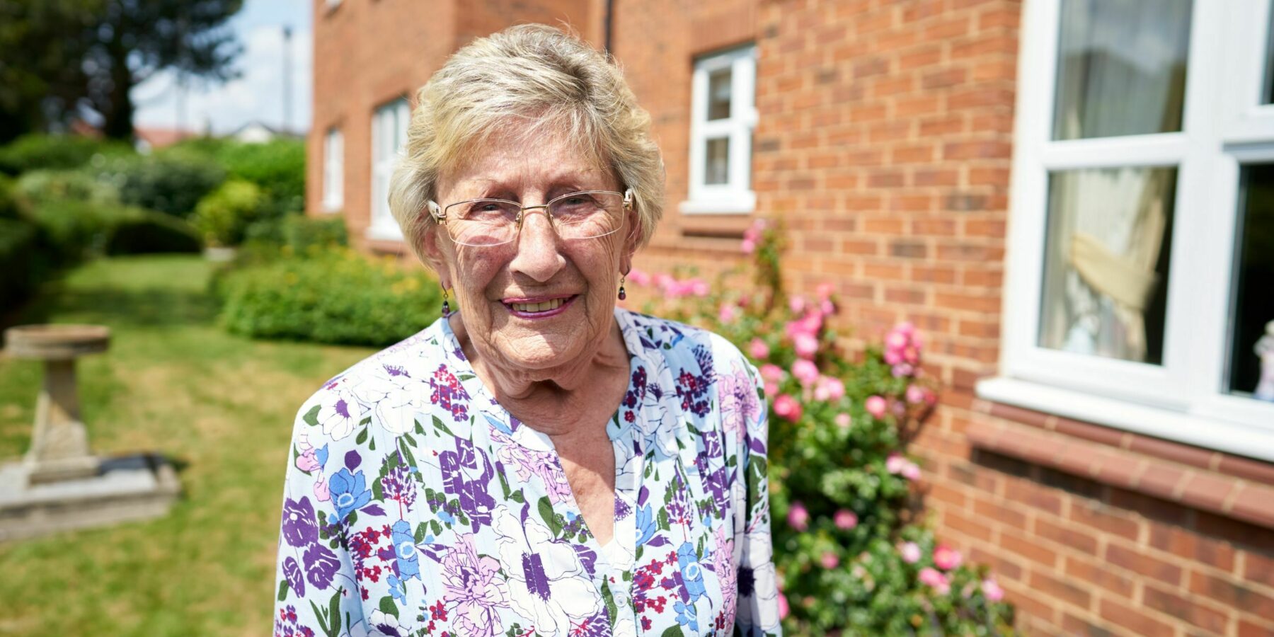 Smiling resident standing near flowers outdoors.