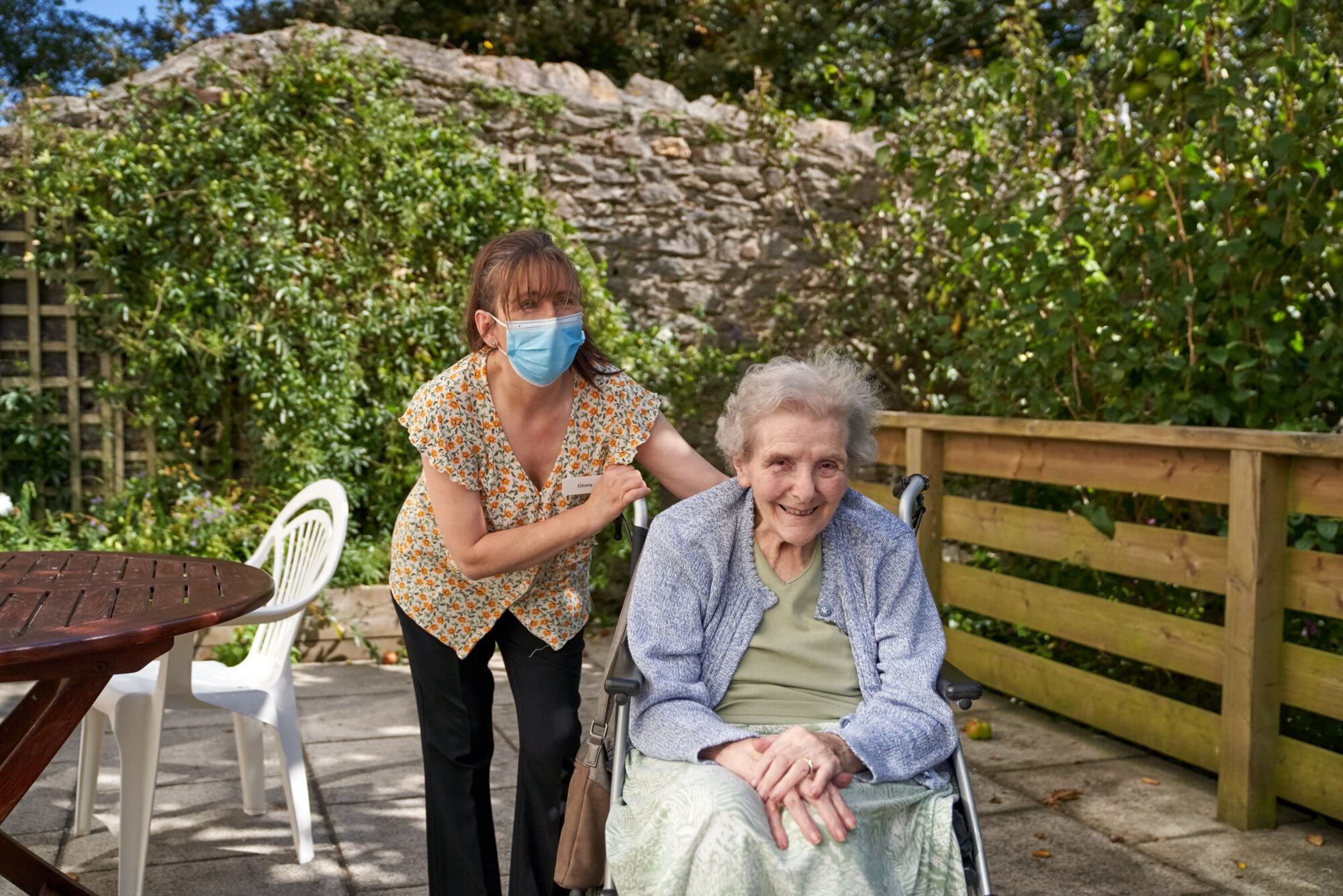 Staff assisting a resident in an outdoor garden area.
