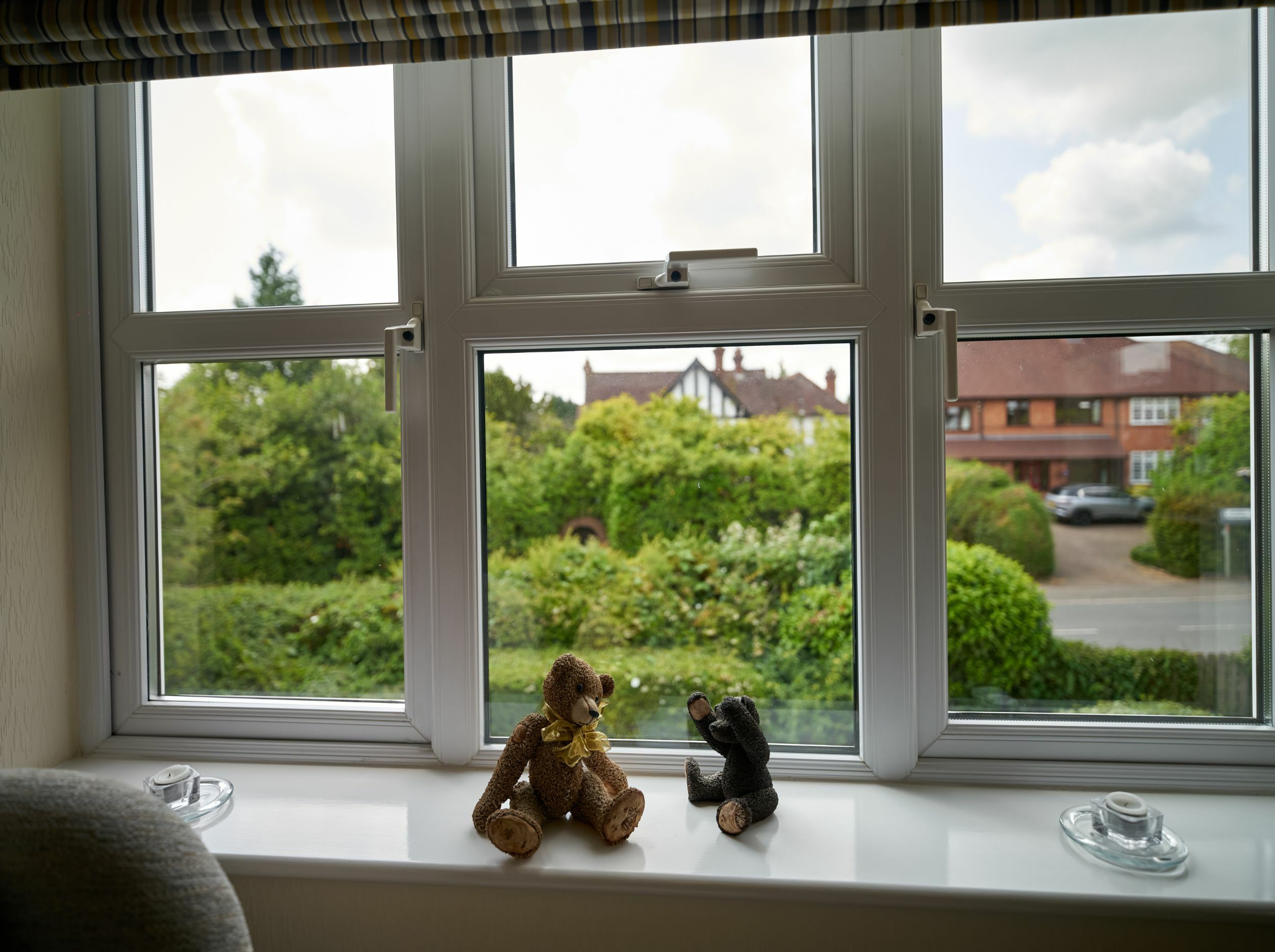 Two teddy bears on a windowsill with greenery outside