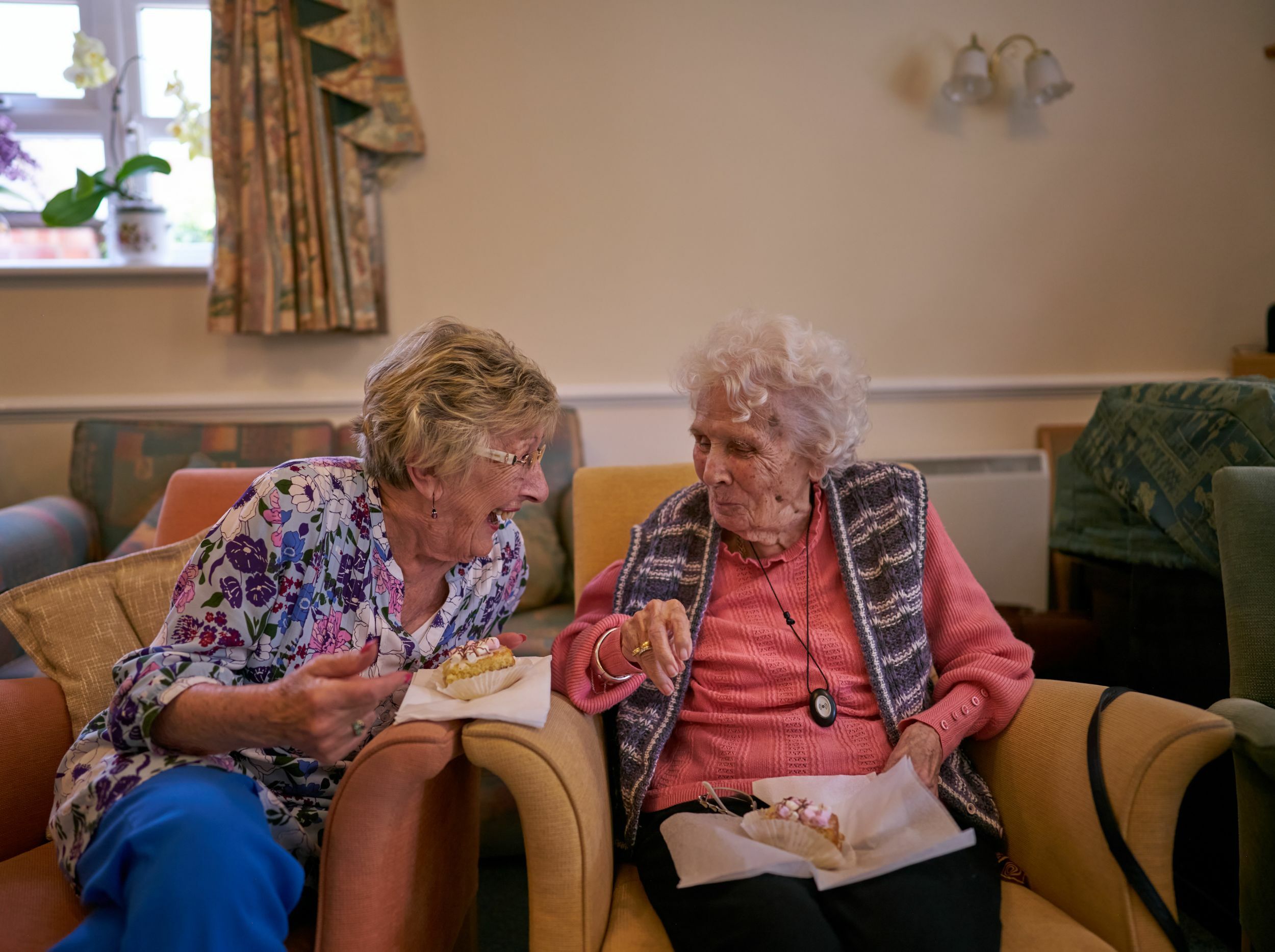 Two elderly women enjoy dessert and conversation.