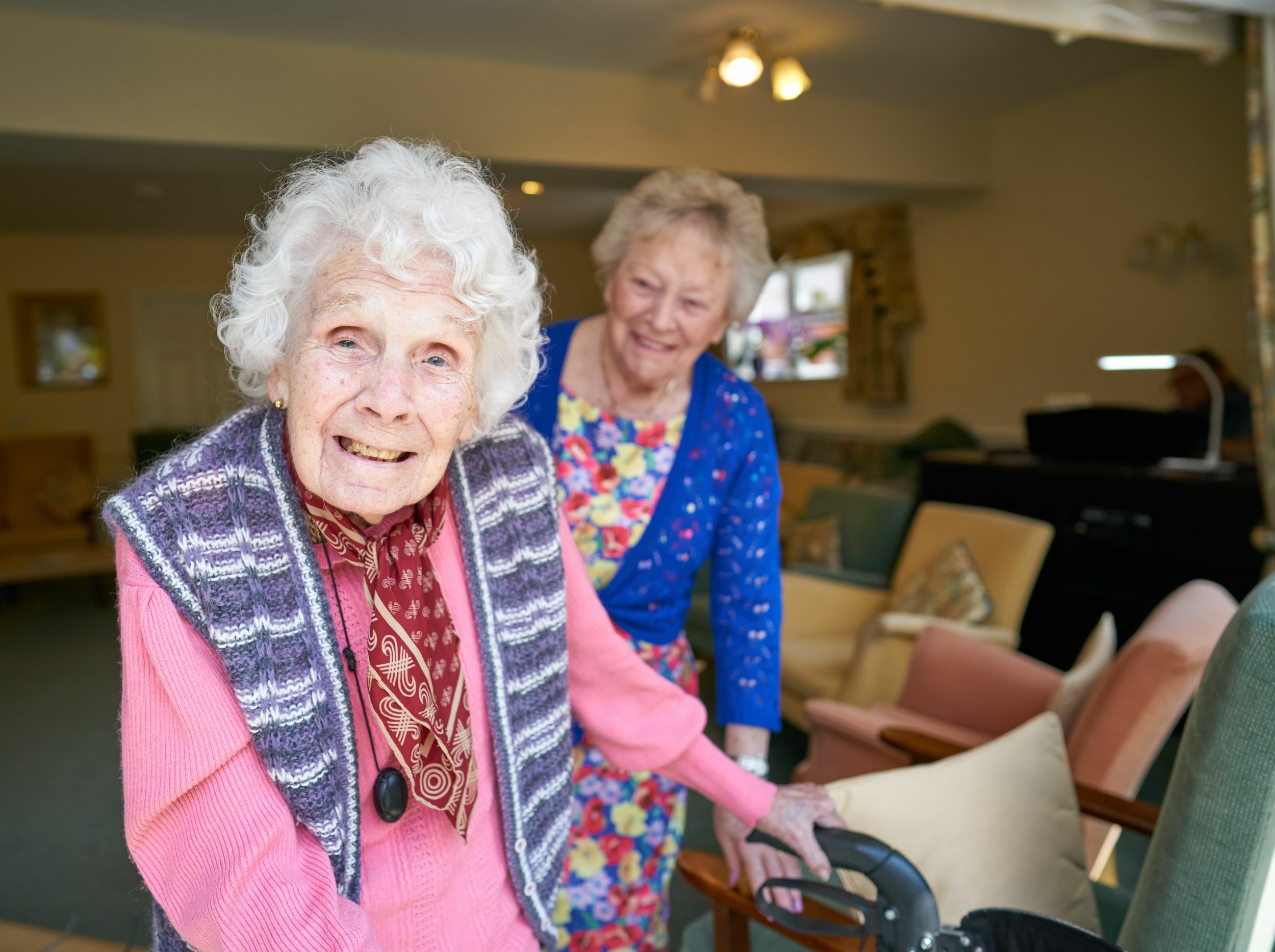Two smiling elderly women interacting in a common area.