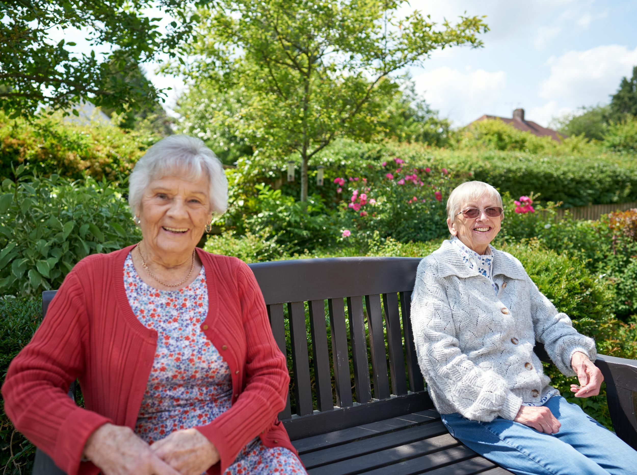 Two elderly women smiling on a garden bench