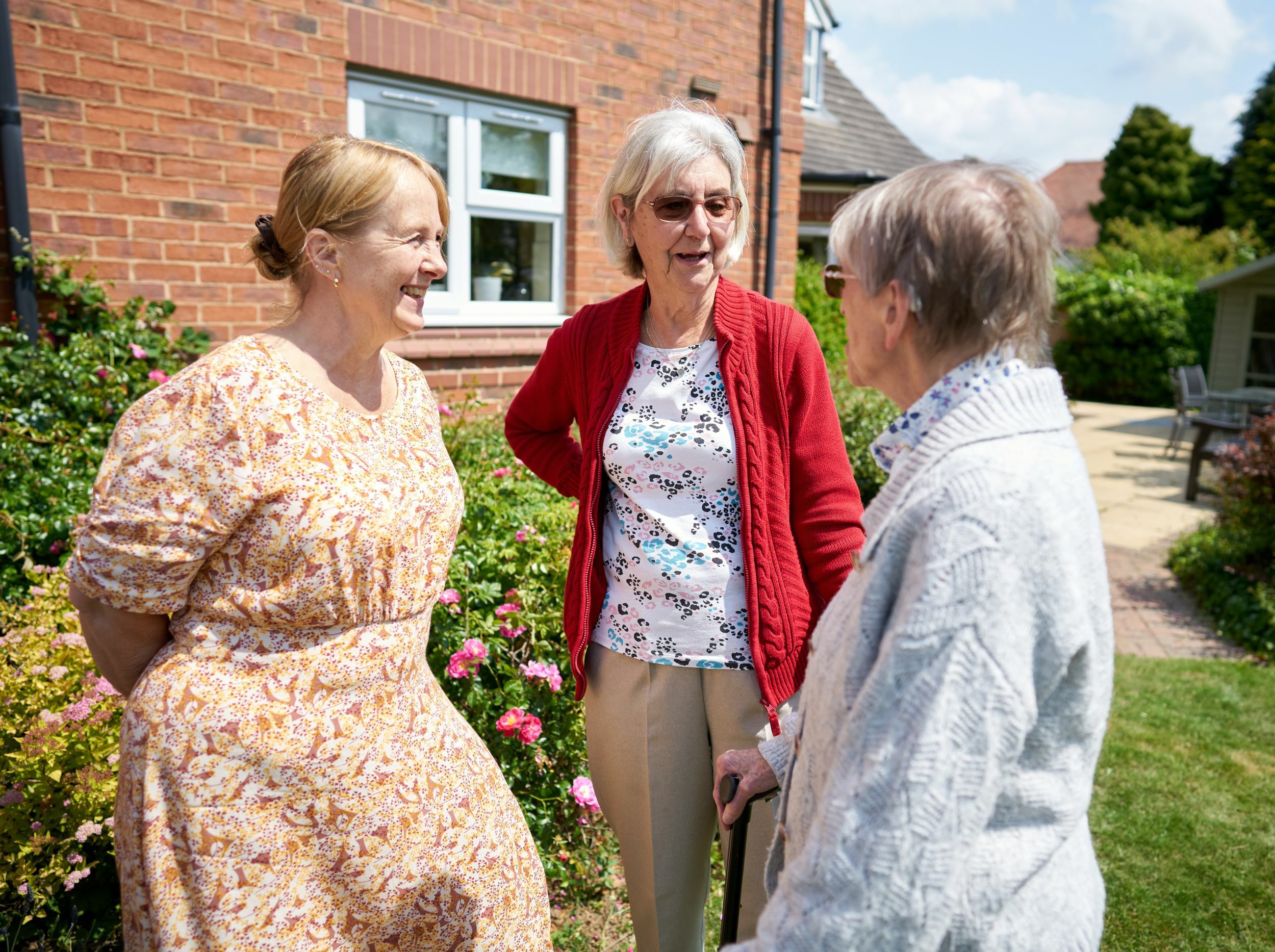 Three women conversing in a garden setting.