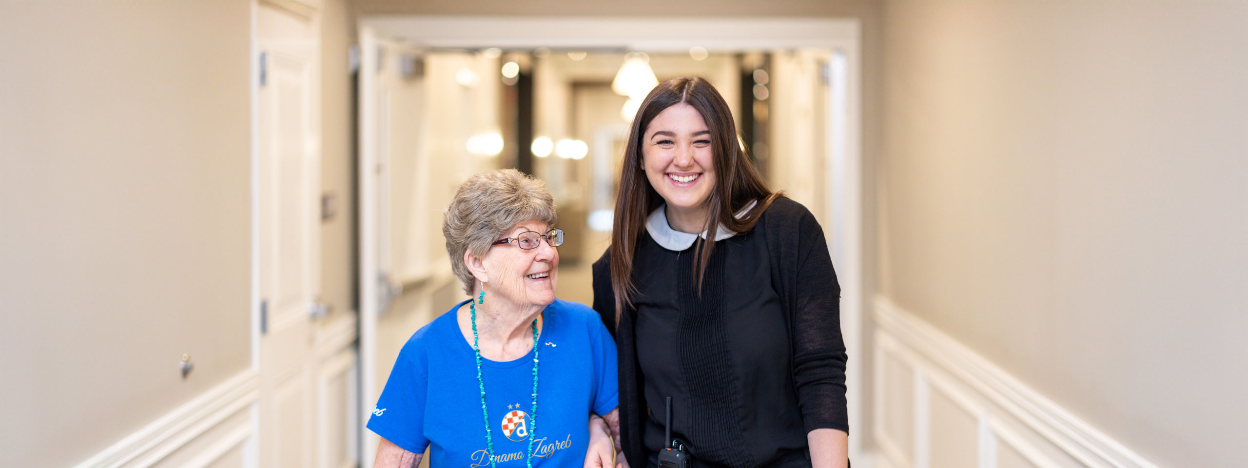 Resident and staff member smiling in a well-lit hallway