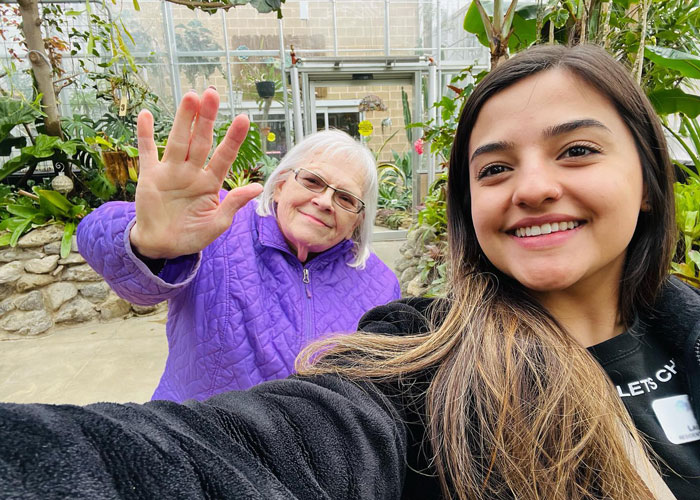 A resident and staff member smiling in a greenhouse