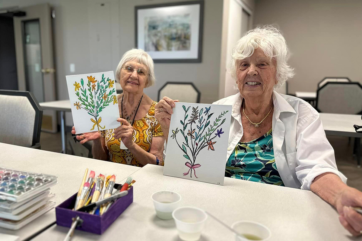 Two residents showing their paintings in an activity room