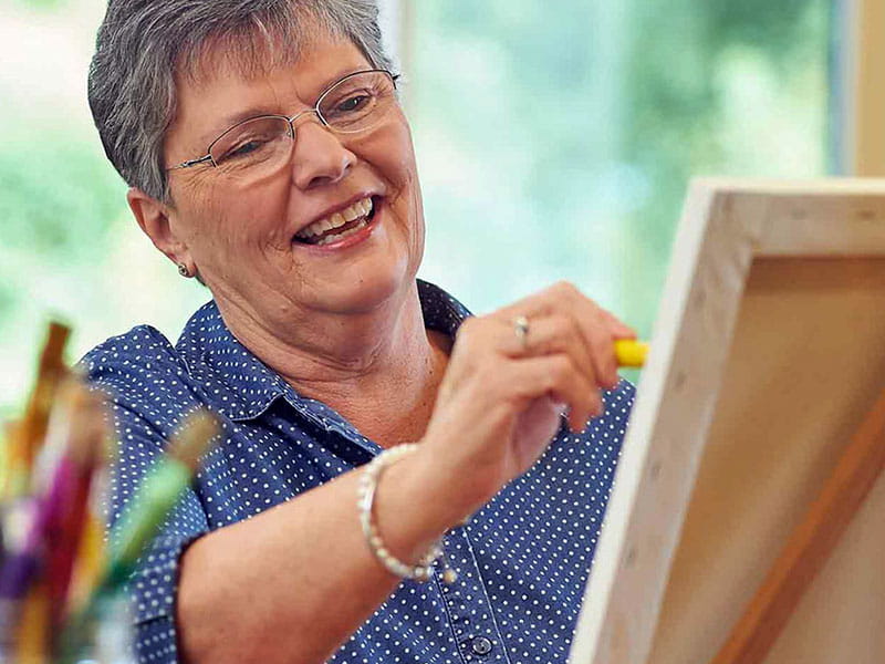 Senior woman painting at an easel in a bright room