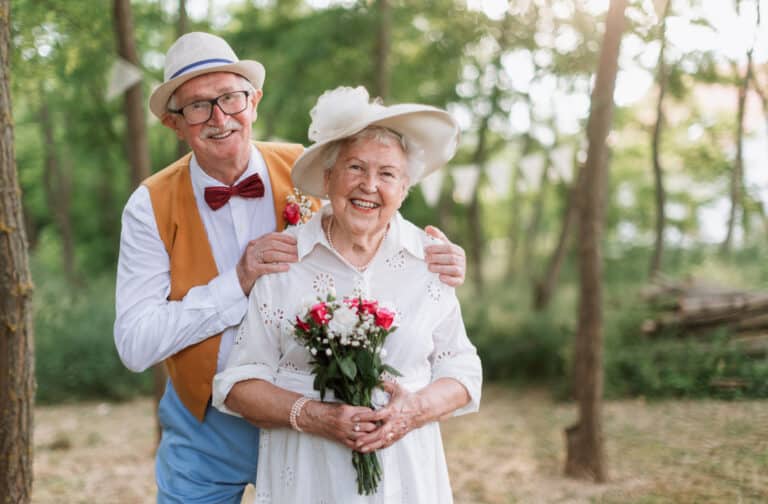 An elderly couple smiling in a forest setting