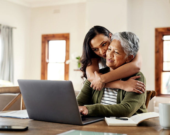 A woman embracing an elderly woman while using a laptop