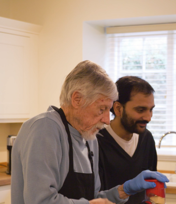 An elderly man cooking with a staff member.