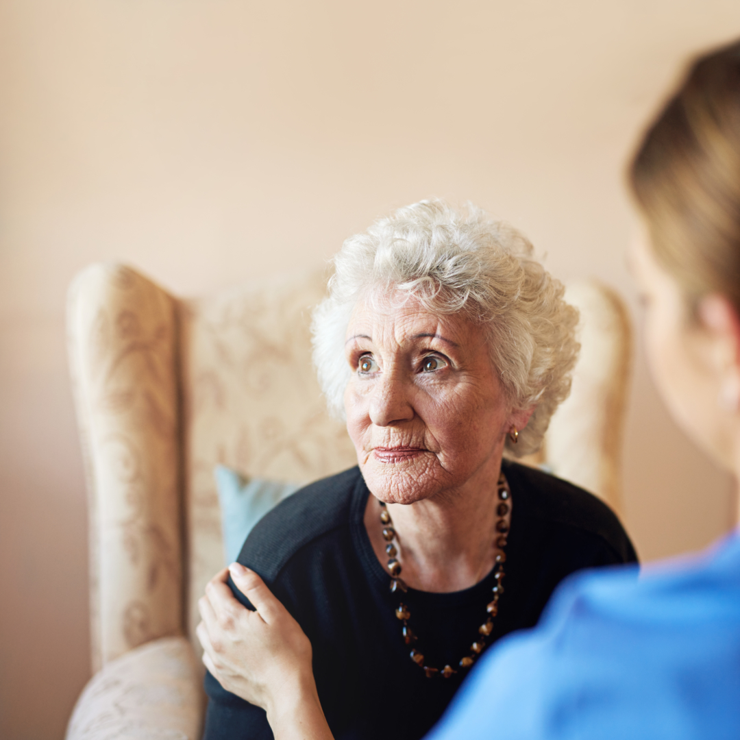 A caregiver interacting with an elderly woman in a cozy interior.