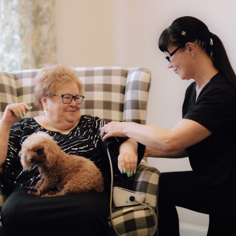 Staff member checking a resident's blood pressure with a dog nearby
