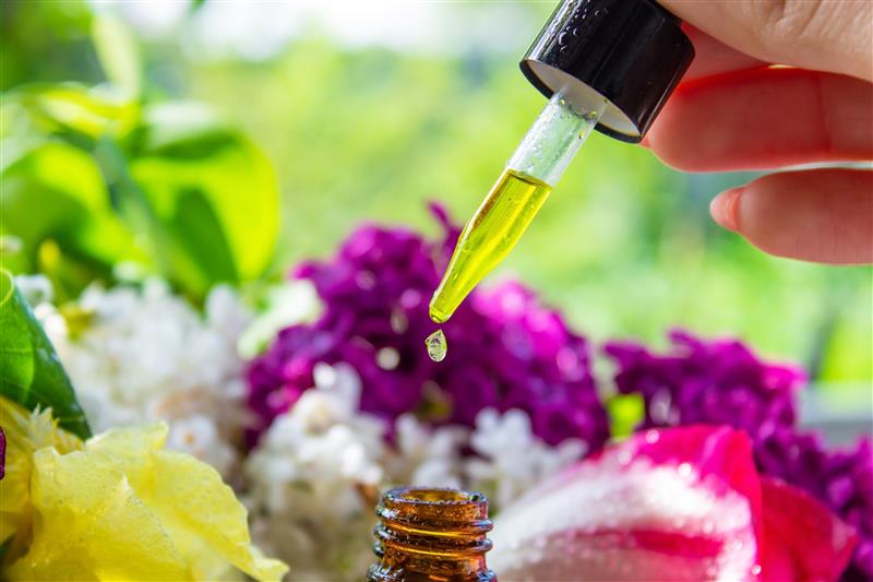 A dropper dispensing oil over flowers and greenery