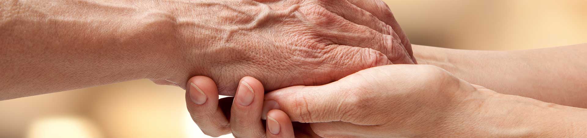An elderly hand held by a younger hand
