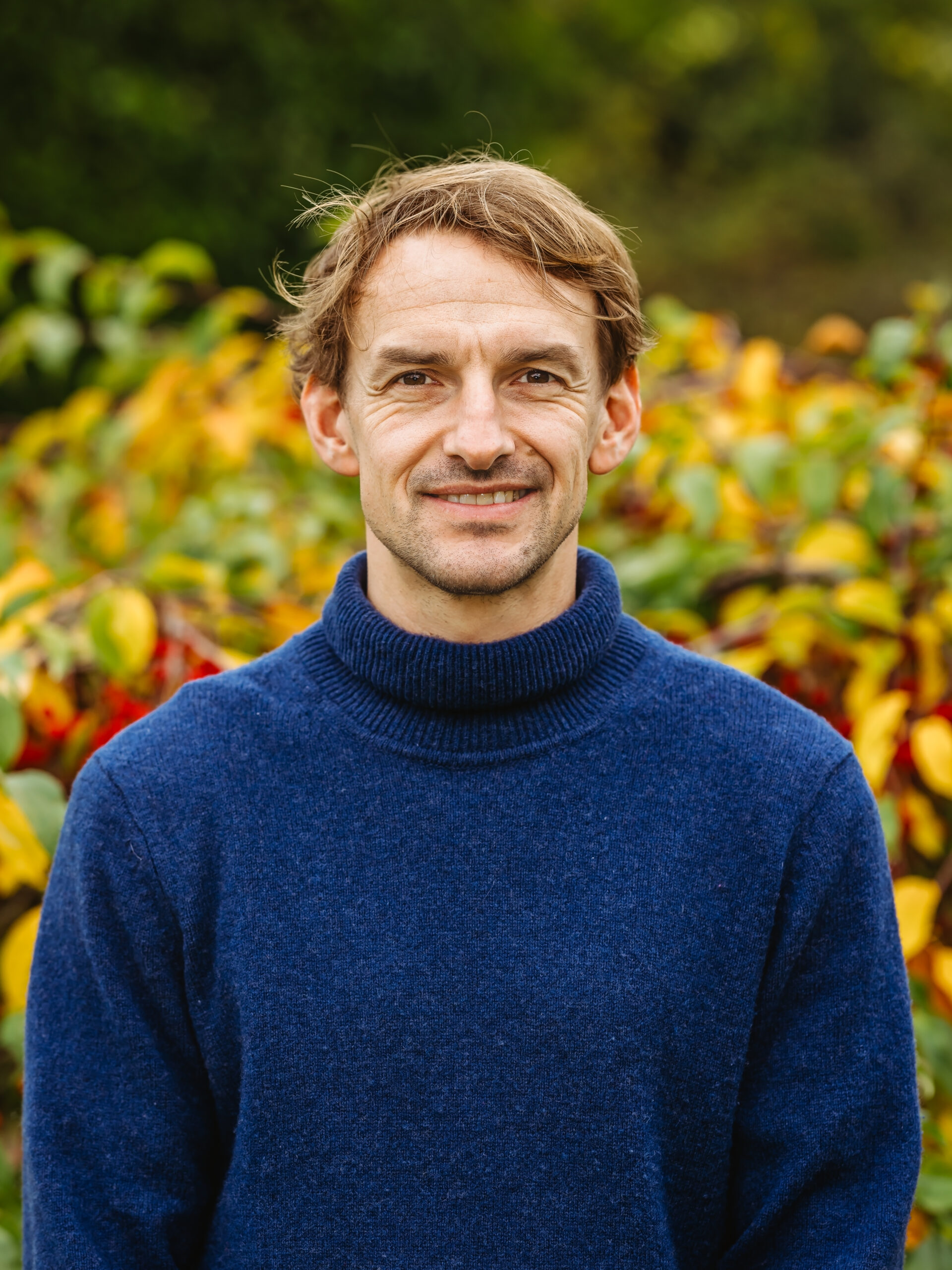 Man smiling in a garden with colorful foliage.