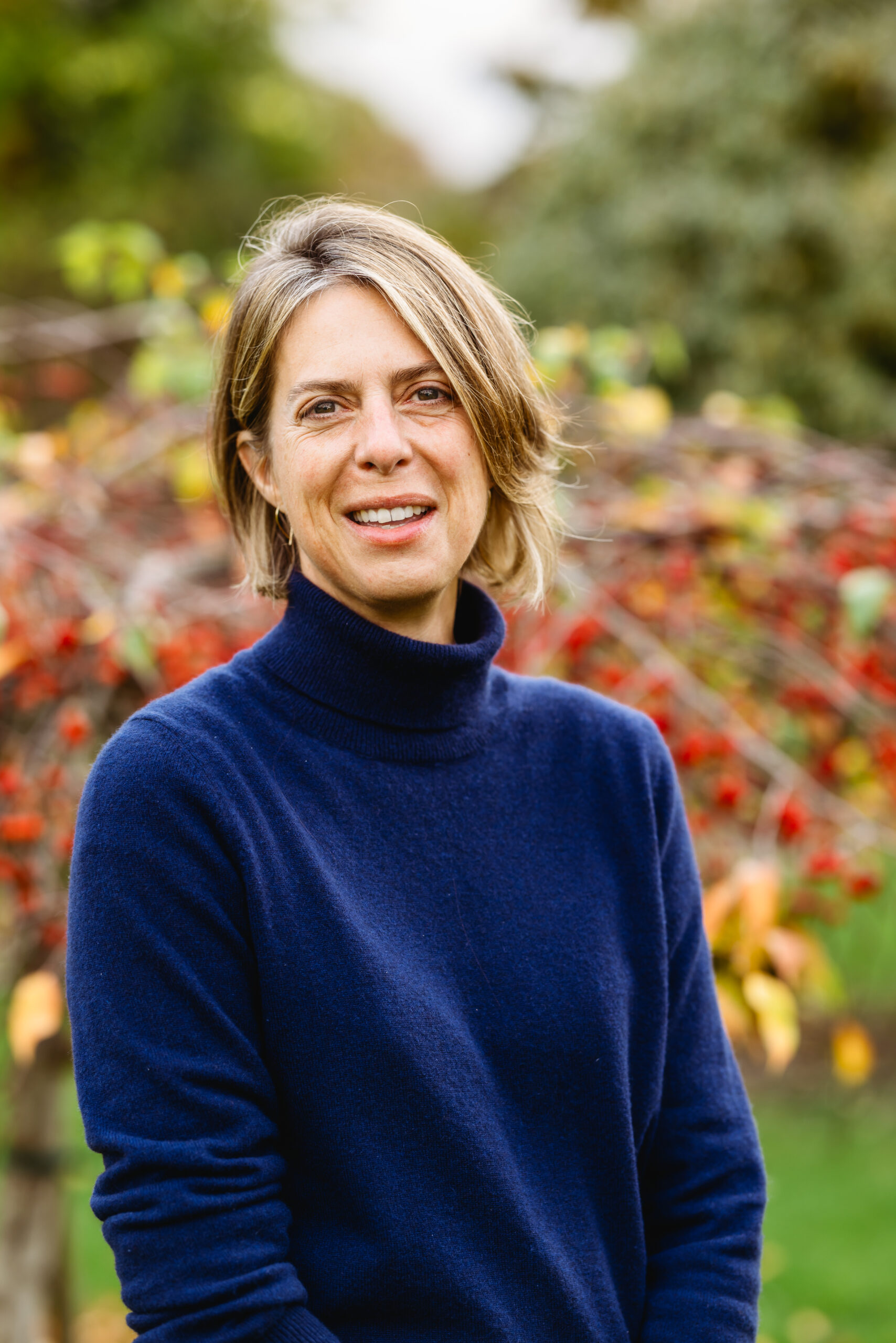 Woman in a navy sweater outdoors with autumn leaves.