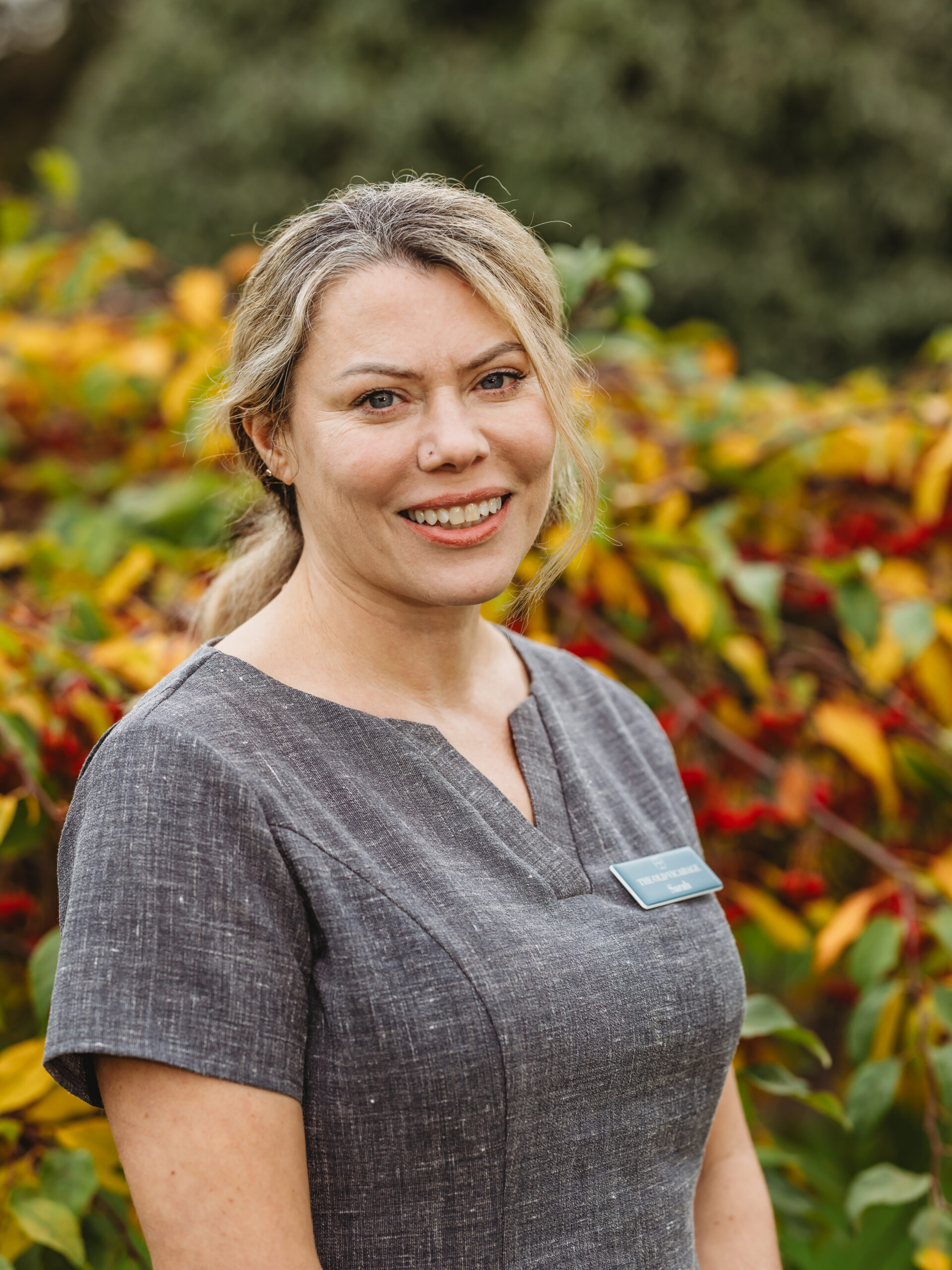 Staff member smiling in front of colorful foliage.