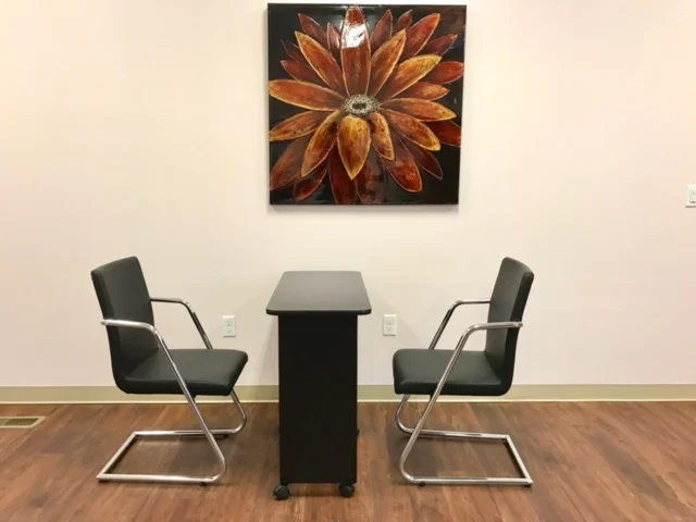 Chairs and table with a floral painting in the background.