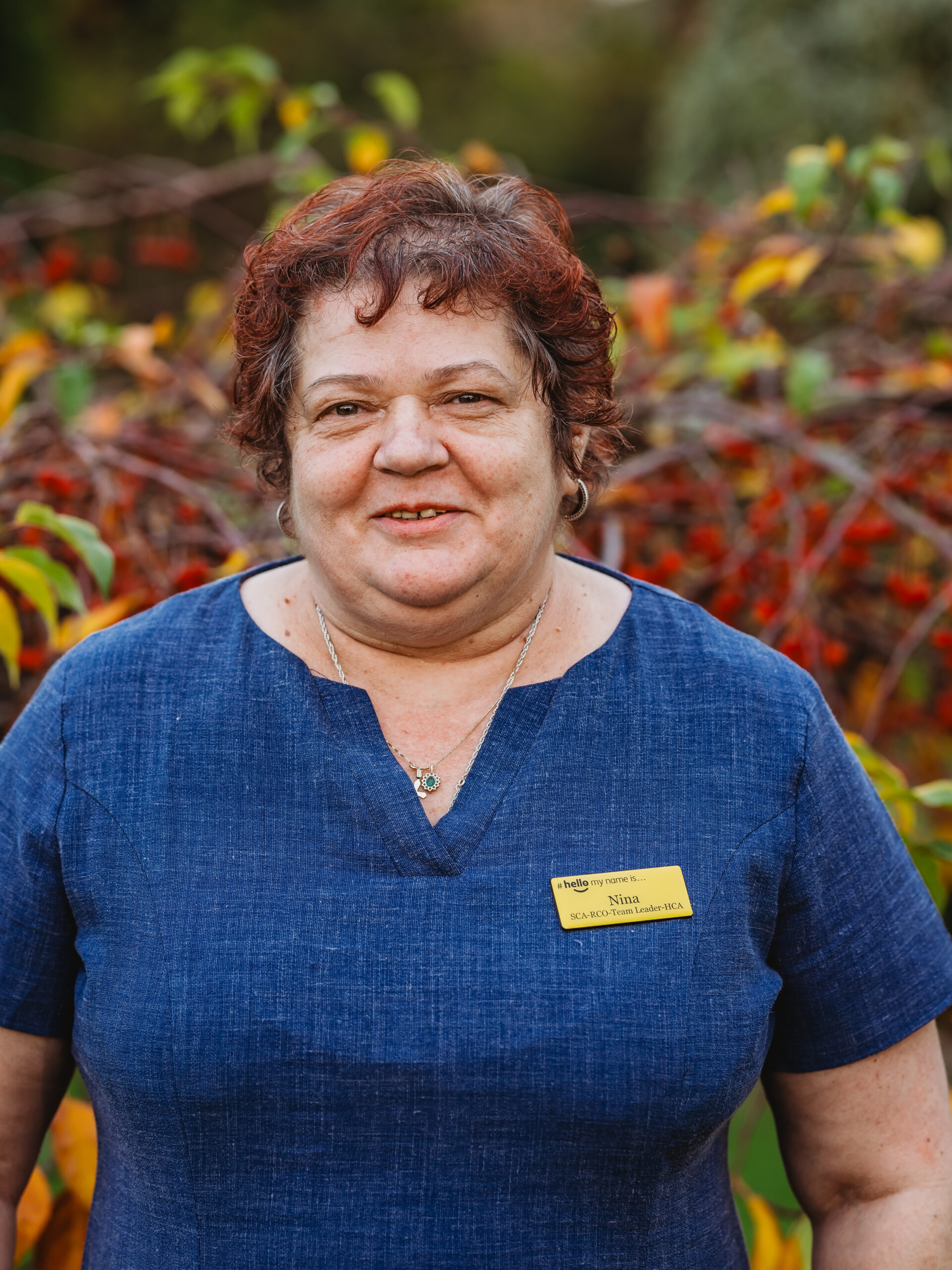 Staff member outdoors with colorful foliage background.