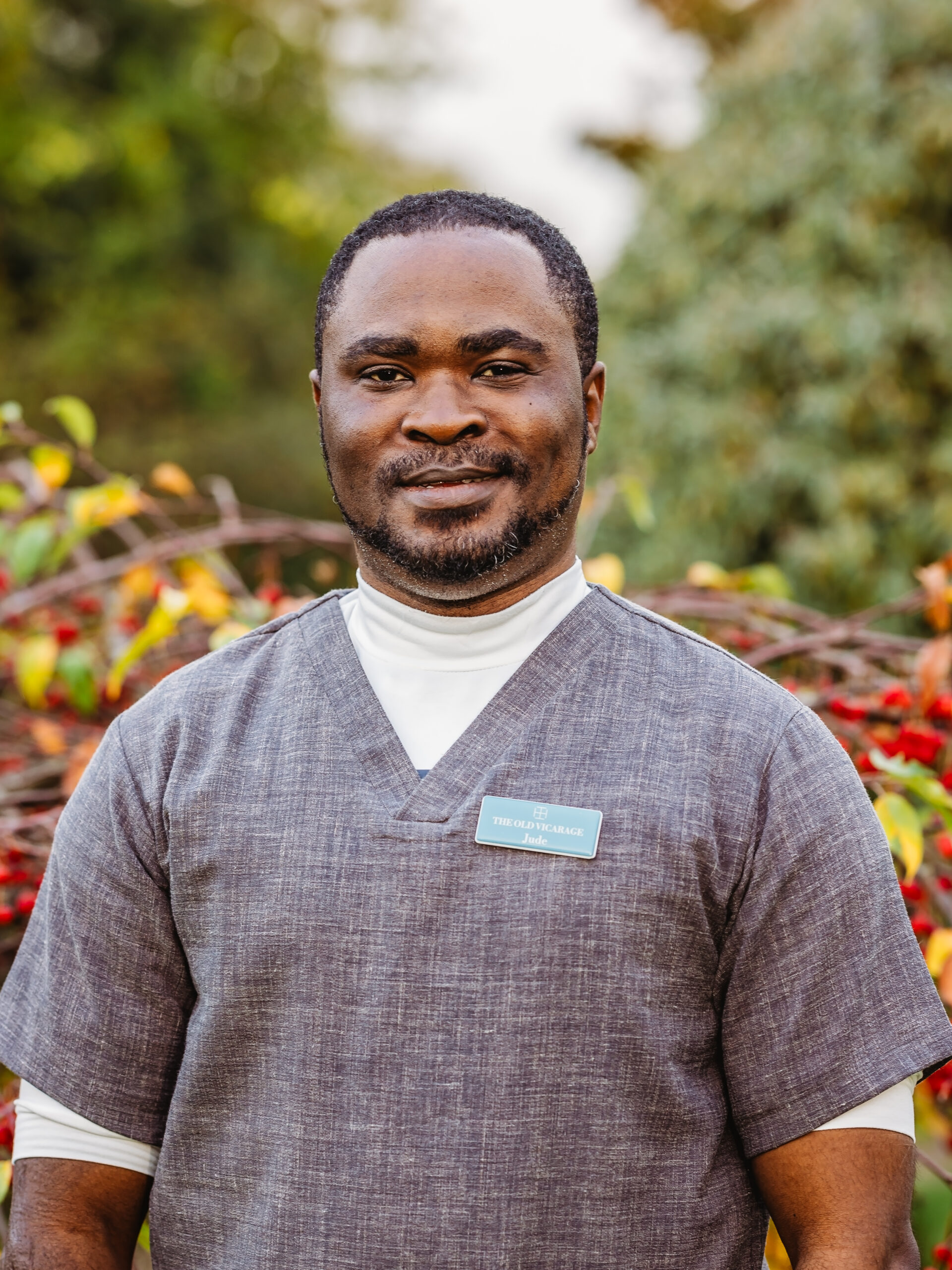 Staff member smiling outdoors in front of foliage.