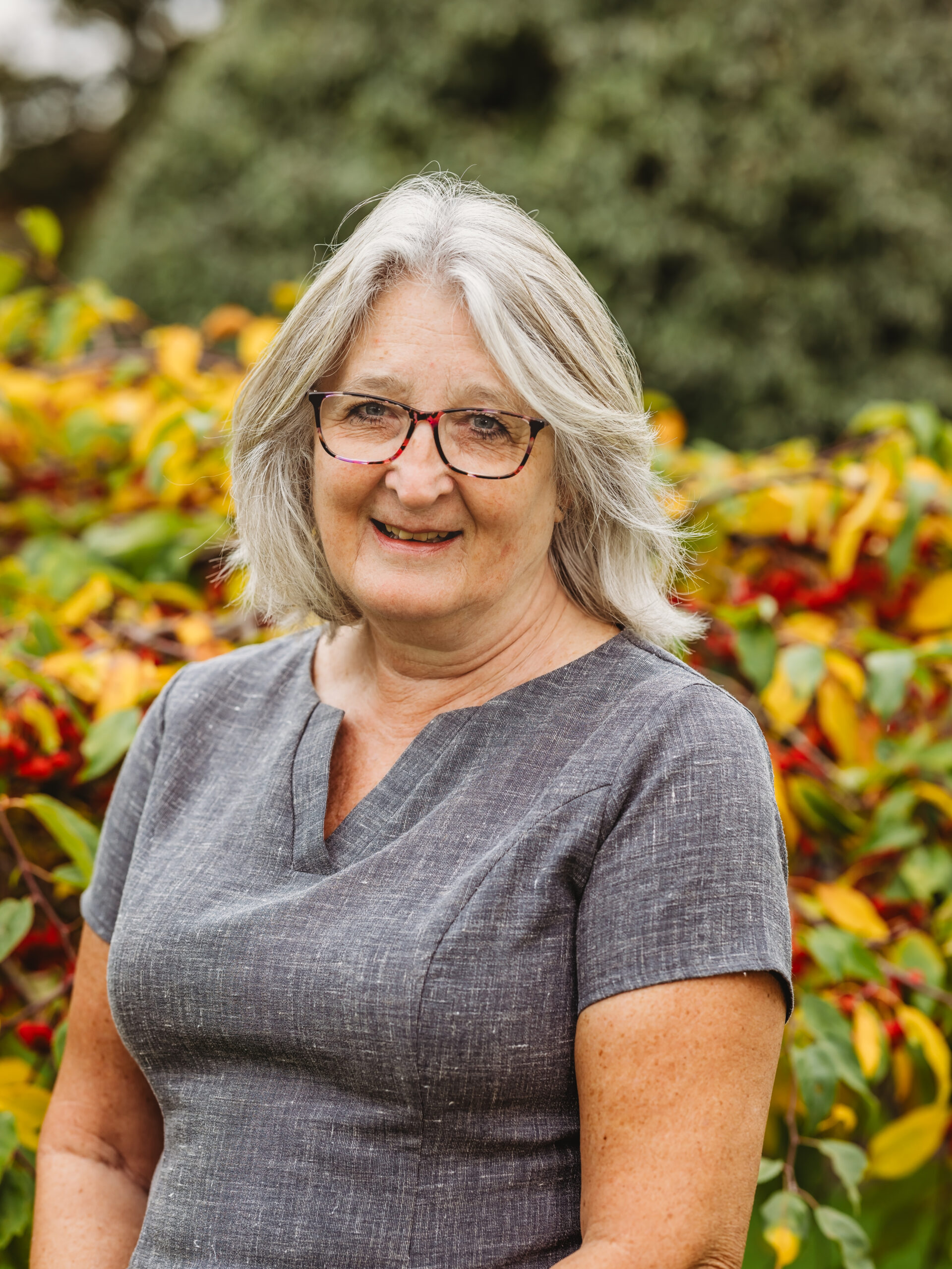 Smiling staff member outdoors with foliage.