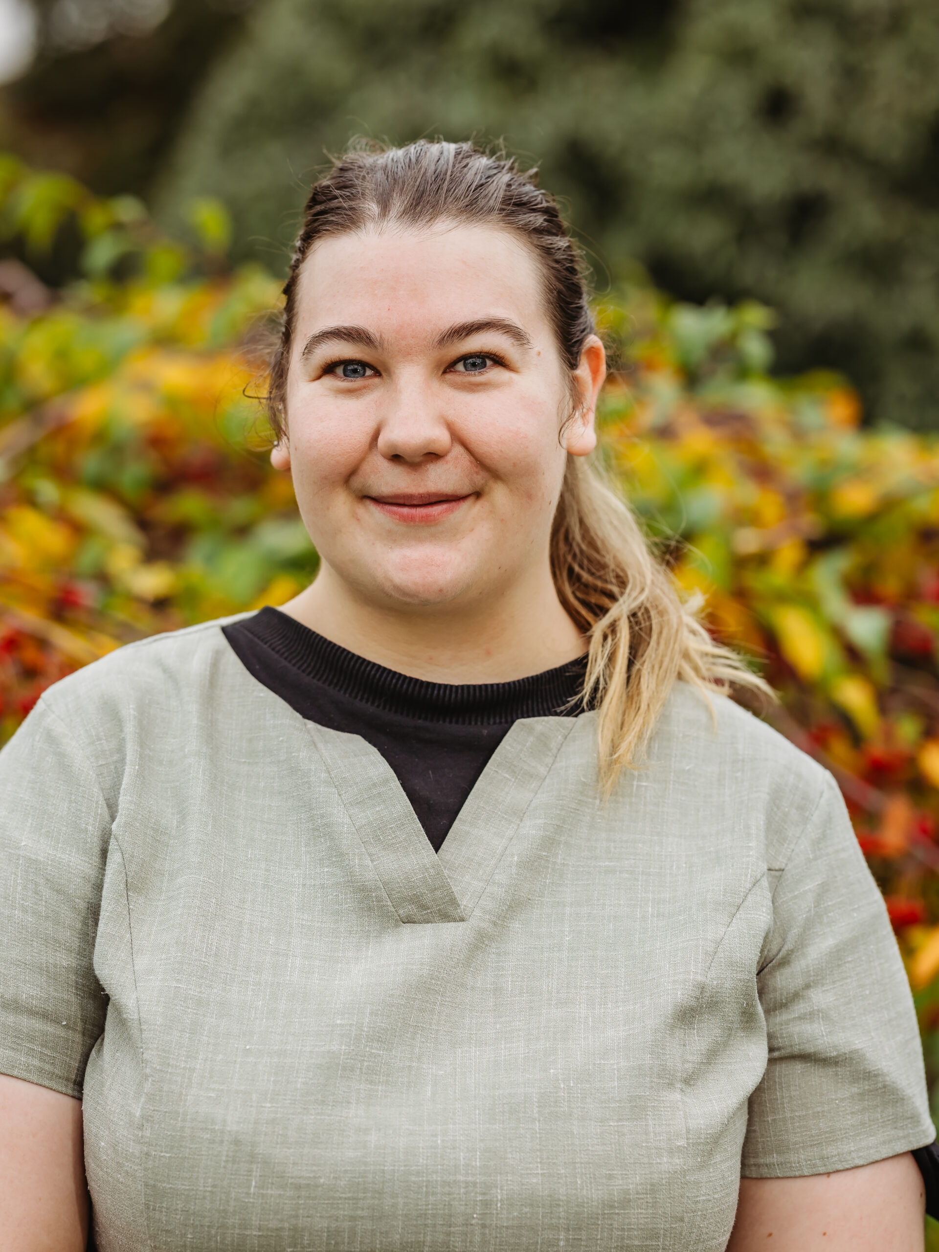 Staff member smiling outdoors among colorful foliage.