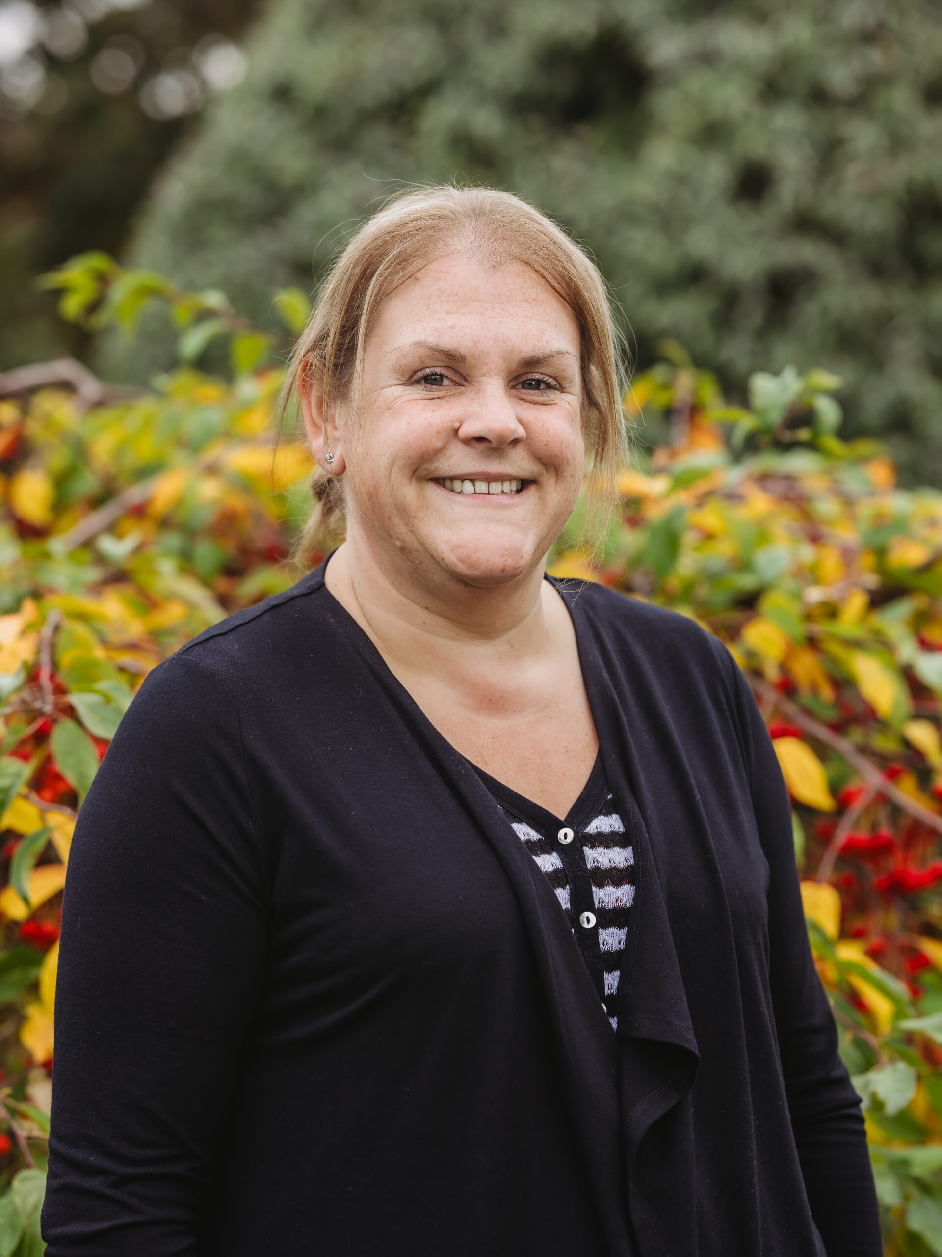 Staff member smiling in front of colorful foliage.