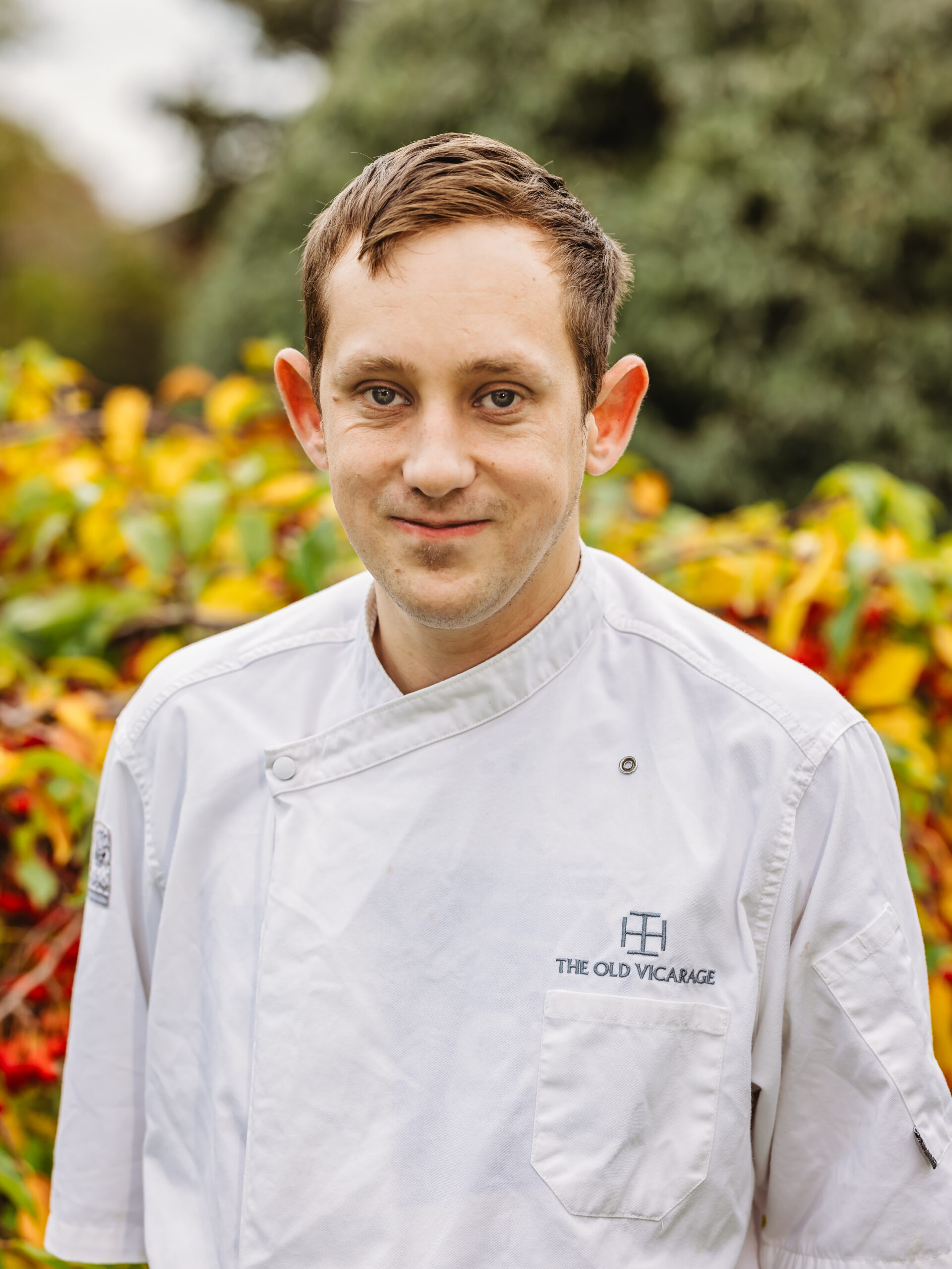 Chef in uniform standing outdoors among greenery