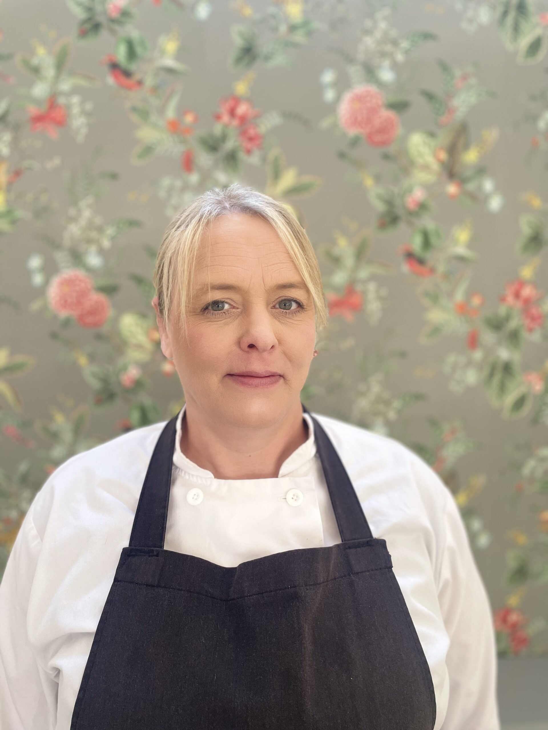 Chef in an apron with floral wallpaper background.