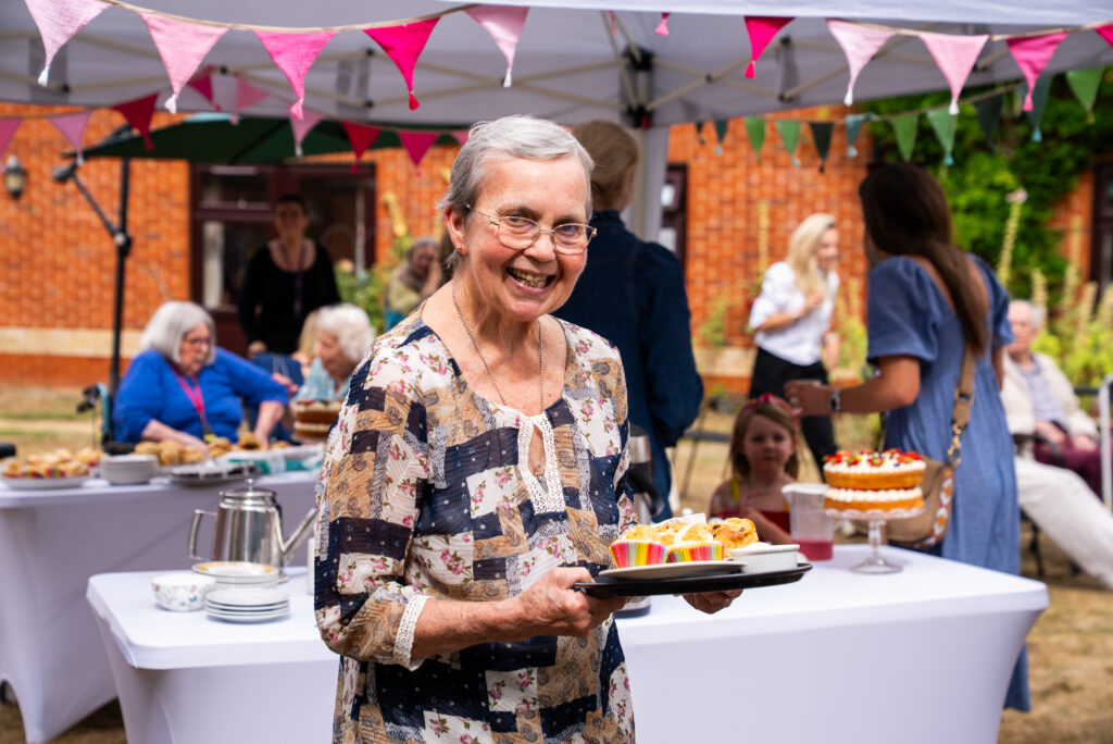 A resident smiling while holding a plate of colorful desserts.