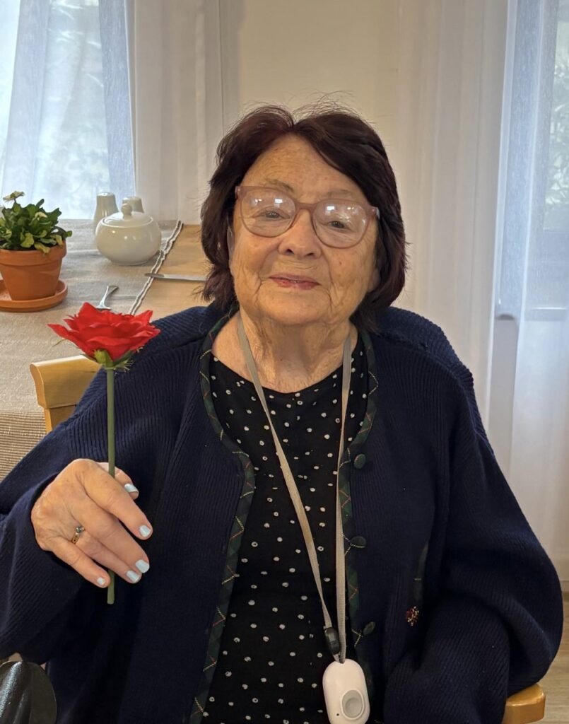 Senior resident holding a red flower indoors.