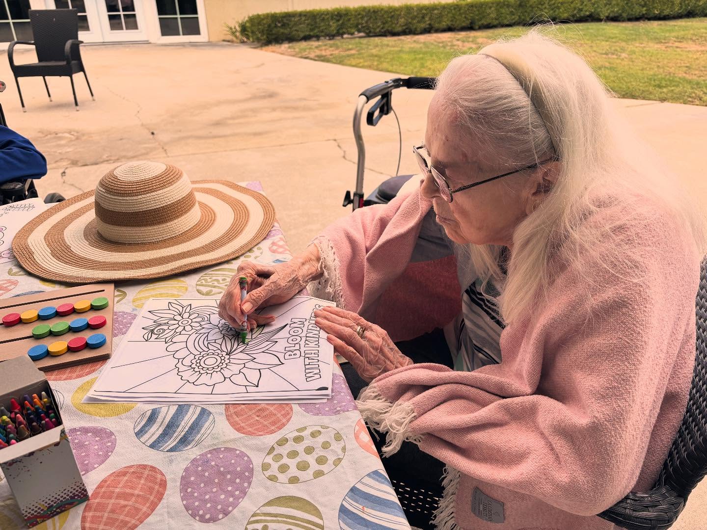 Elderly woman coloring outdoors at a table.
